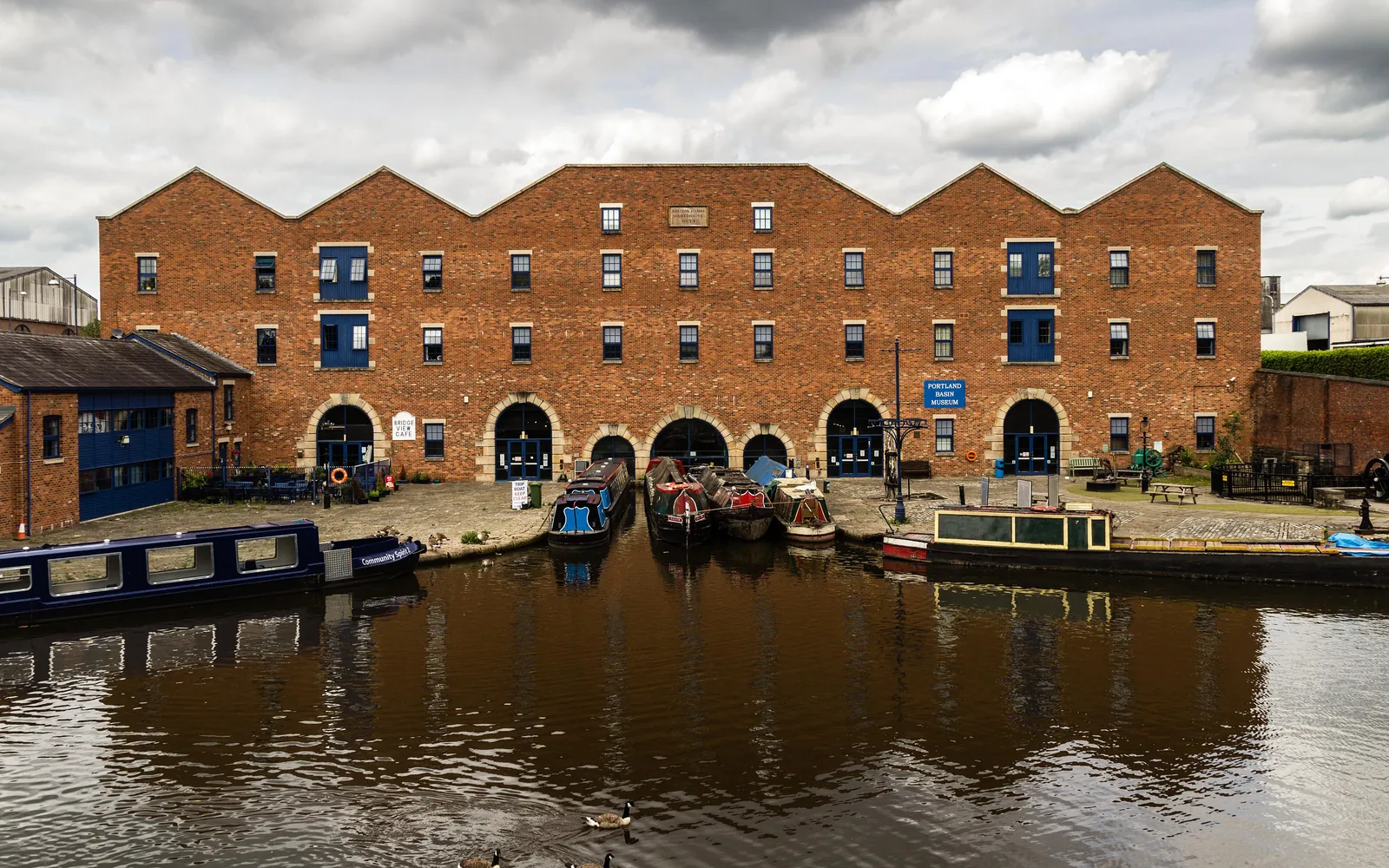 A restored brick canal warehouse with narrowboats moored in front at Portland Basin