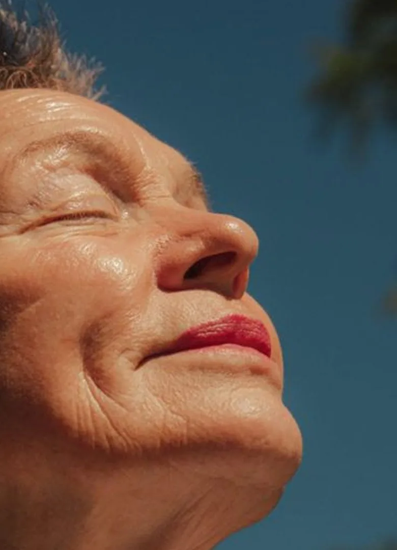 An older woman with her eyes closed, smiling in the sunshine